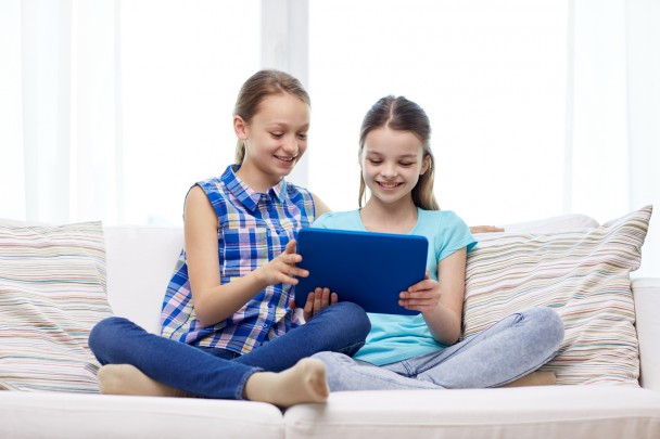 happy girls with tablet pc sitting on sofa at home
