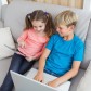 Happy siblings using laptop and tablet pc on sofa at home in the living room