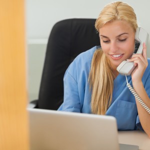 Blonde nurse calling next to a laptop in hospital reception
