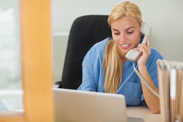 Blonde nurse calling next to a laptop in hospital reception