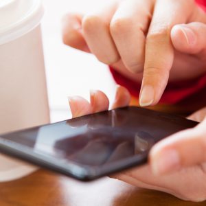 Close-up of hand using cell phone near disposable cup