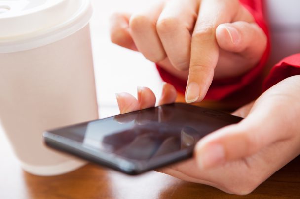 Close-up of hand using cell phone near disposable cup
