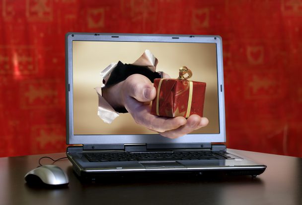 man hand with a christmas  gift come out from a screen of a laptop computer