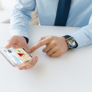 business, technology, navigation and people concept - close up of male hand holding and showing transparent smart phone and watch at office with gps navigator map on screen