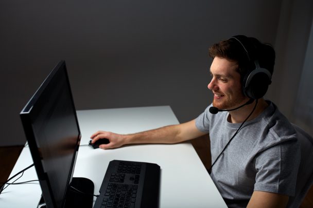 technology, gaming, entertainment, let's play and people concept - happy young man in headset with pc computer playing game at home and streaming playthrough or walkthrough video